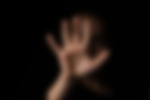 Imagem desfocada mostrando a silhueta de uma mão aberta contra um fundo totalmente escuro. Os dedos estão estendidos em um gesto que sugere pare, socorro ou apoio contra uma superfície transparente.