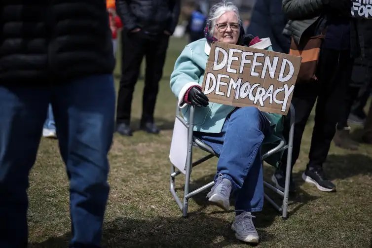 79-year-old Christine Hughes holds a sign as she attends a demonstration during the day of 