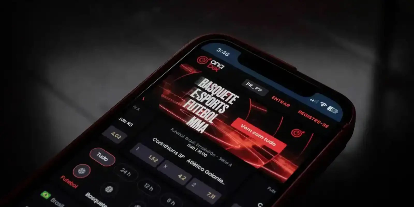 Fotografia aproximada de um smartphone com tela escura exibindo o aplicativo de apostas esportivas Onabet. Na interface vermelha e preta, destacam-se as categorias "Basquete, E-sports, Futebol, MMA", além de opções de apostas para uma partida de futebol entre Corinthians e Atlético Goianiense com cotações (odds) visíveis na tela.