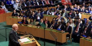 Fotografia de imprensa que mostra o presidente do Brasil, Luiz Inácio Lula da Silva, discursando na tribuna principal da Assembleia Geral das Nações Unidas, em Nova York. Ele veste terno escuro com gravata e está posicionado atrás do púlpito oficial, onde se veem os microfones e o brasão dourado da ONU, enquanto se pronuncia diante dos líderes mundiais.