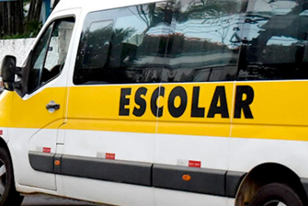 Lateral de uma van de transporte escolar branca com uma faixa amarela horizontal onde está escrita a palavra "ESCOLAR" em letras maiúsculas pretas.