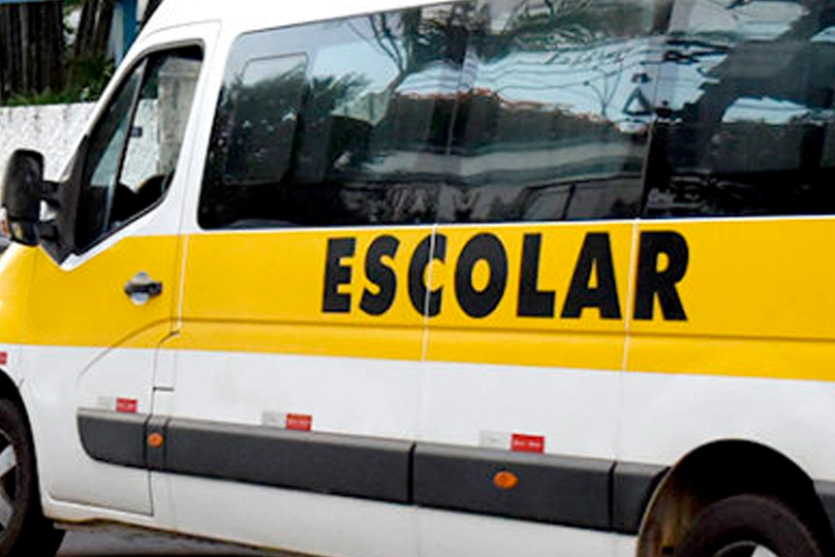 Lateral de uma van de transporte escolar branca com uma faixa amarela horizontal onde está escrita a palavra "ESCOLAR" em letras maiúsculas pretas.